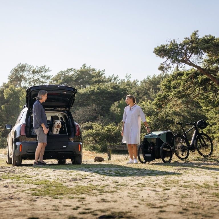 A man and woman stand by the back of a car while a dog sits in a Thule Allax dog crate with the door open.