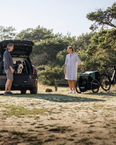 A man and woman stand by the back of a car while a dog sits in a Thule Allax dog crate with the door open.
