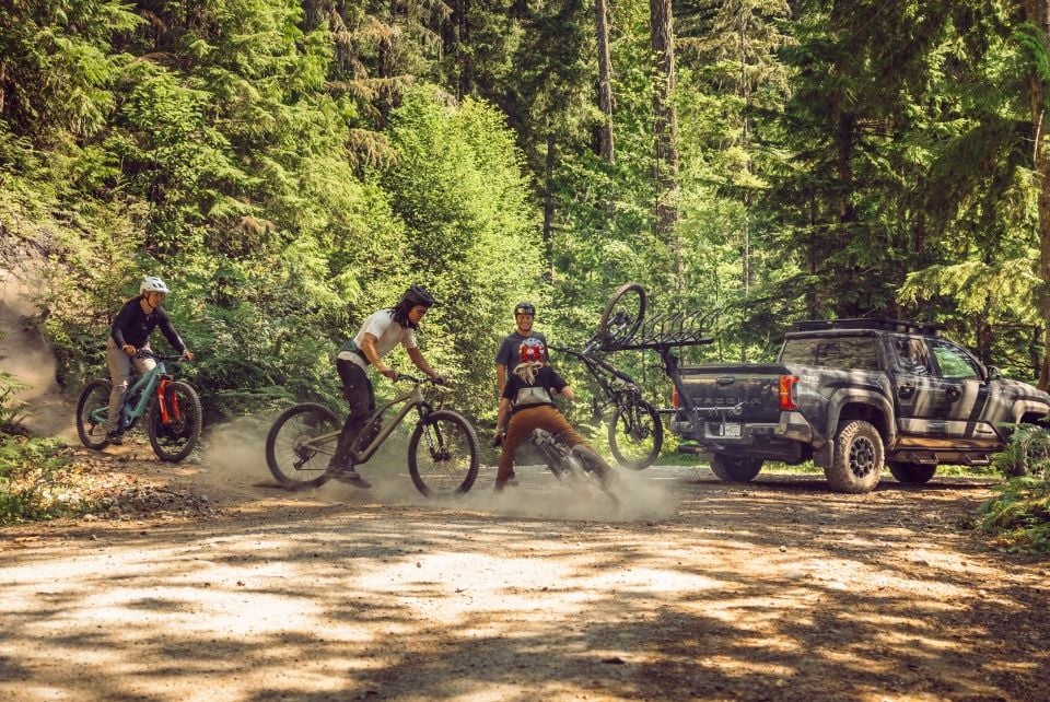 A group of mountain bikers gather around a pickup truck with a Thule ReVert bike carrier. 