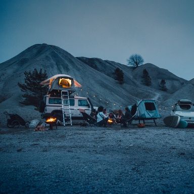 People sit around a campfire in the dusk next to two vehicles equipped with Thule tents and products.