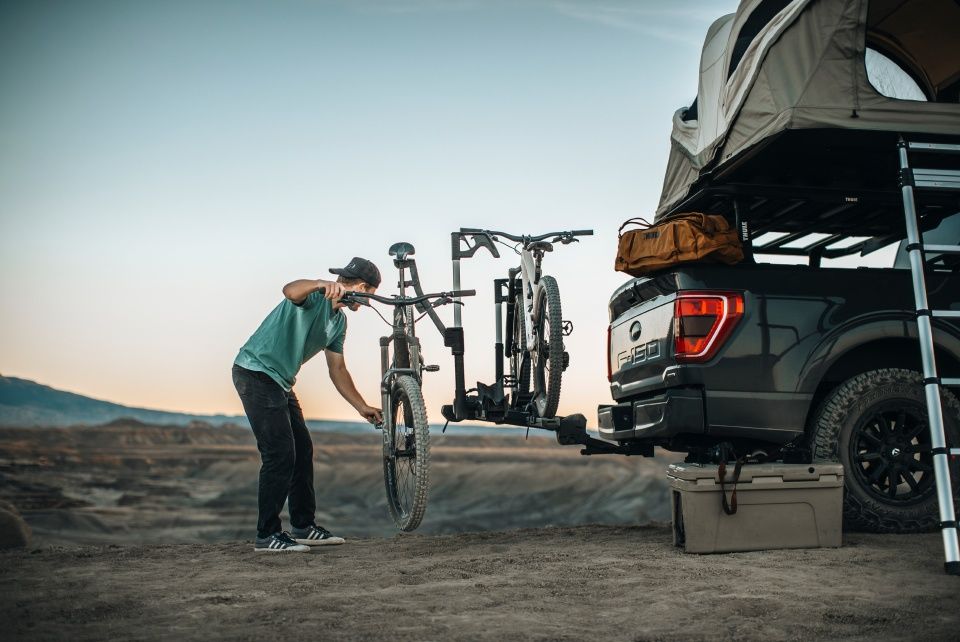 A man unloads a bike from the Thule Verse hitch mounted bike rack which is attached to a truck.