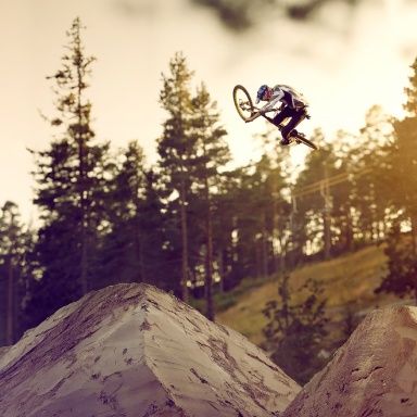 A man on a bike flies through the air while doing a trick at an outdoor bike park.